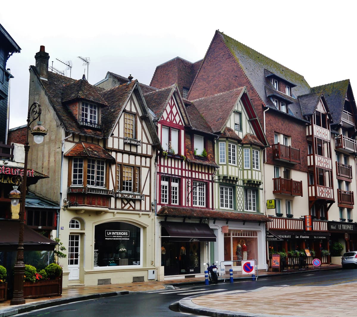 Angle de rue bordé de maisons à pans de bois peints en blanc, rouge et vert, toits d'ardoise et de tuiles percés de lucarnes, balcons de bois et vitrines au rez-de-chaussée.