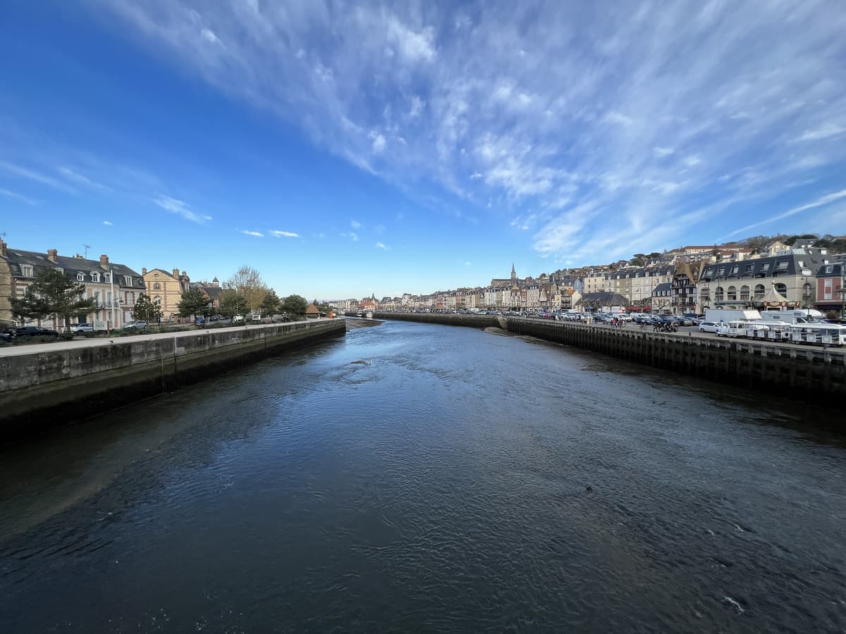 La rivière entre deux quais de pierre, sous un ciel bleu strié de nuages, avec des immeubles et un clocher au loin.